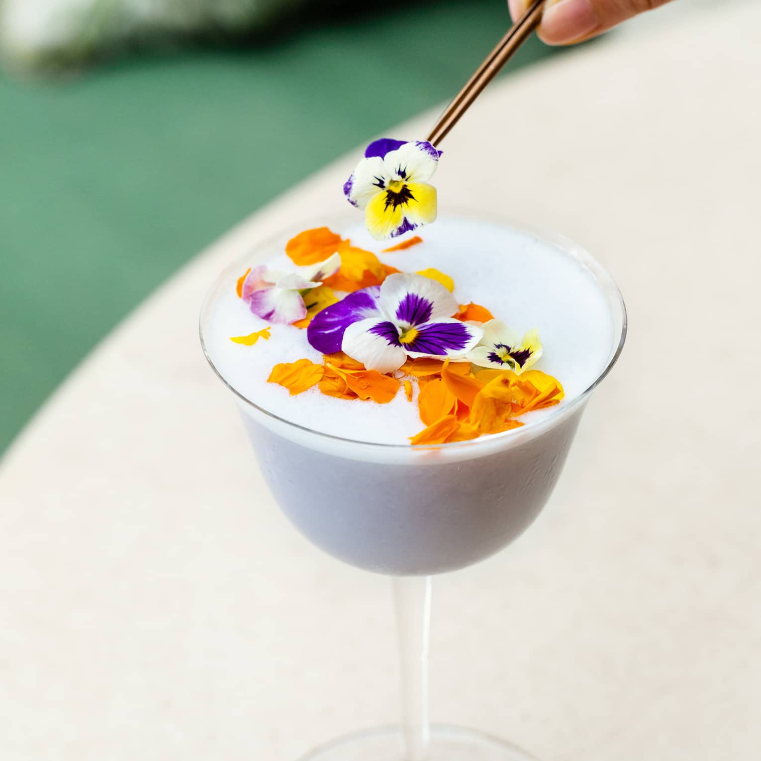 A stemmed glass of a white tropical cocktail topped with flowers 