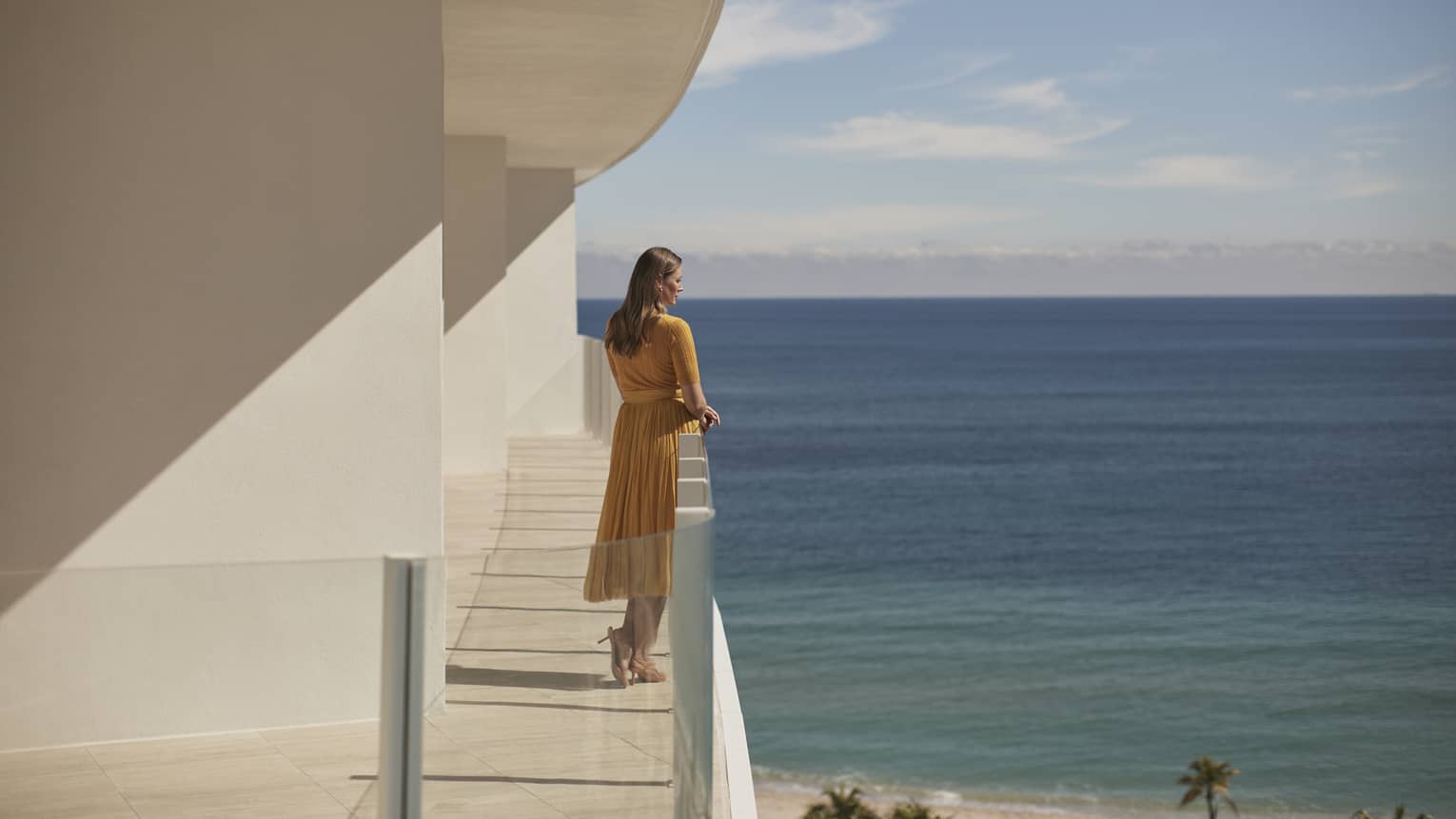 A woman standing on a balcony of a white stone building with the ocean in the background.
