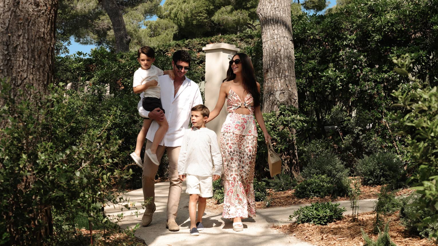 A family walks along a shaded path surrounded by lush green trees