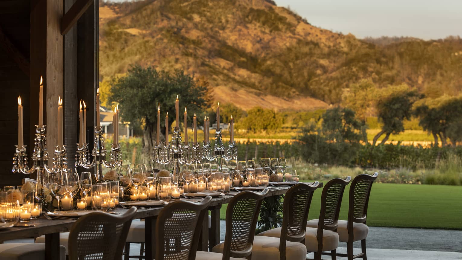 A long table with candles outside near mountains.