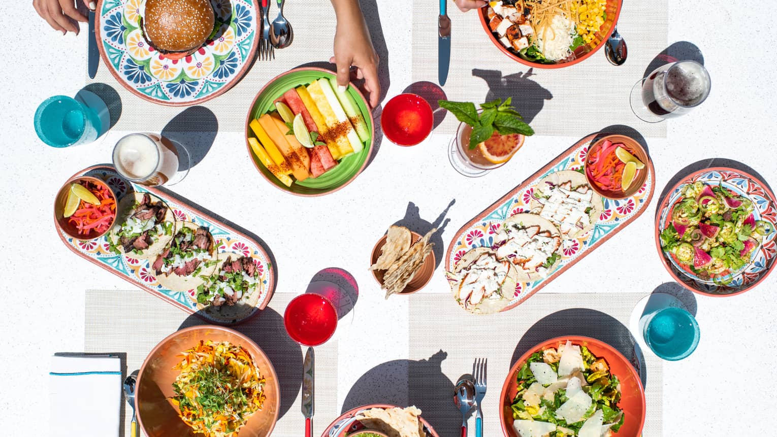 From above, a white dining table filled with colorful small plates, blue and red cups
