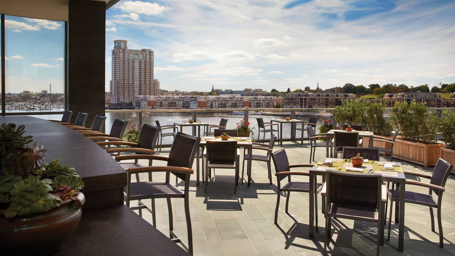 Bar with stools, tables and chairs on sunny patio with harbour view 