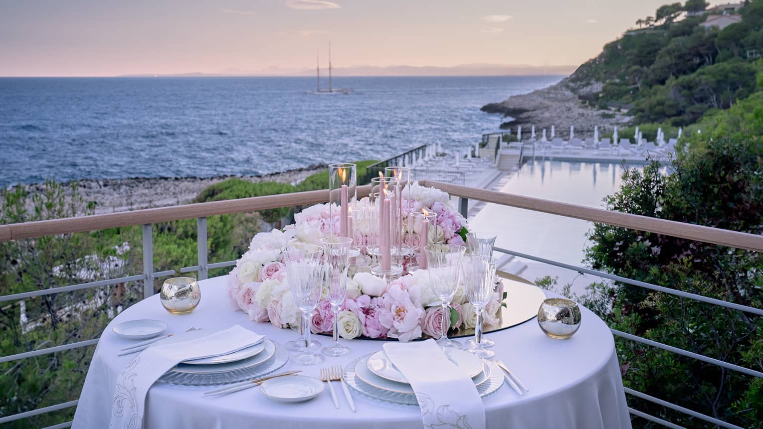 Balcony with round set table, pink floral arrangement, water views at sunset