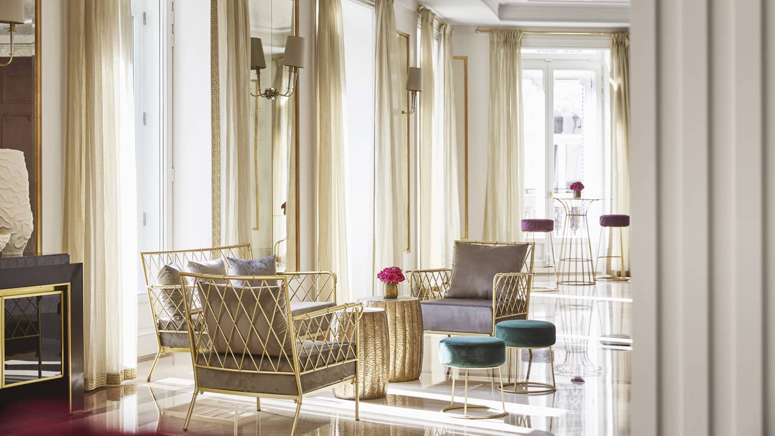 A light-filled room with chairs as well as stools and tables of various heights and floor-to-ceiling windows with beige curtains open to let in natural light