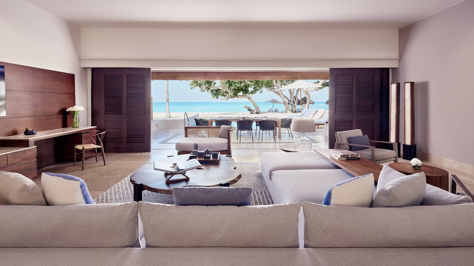 Arena Beach House living room with cream sectional sofa, large oak coffee table, doors open to outdoor dining area and pool