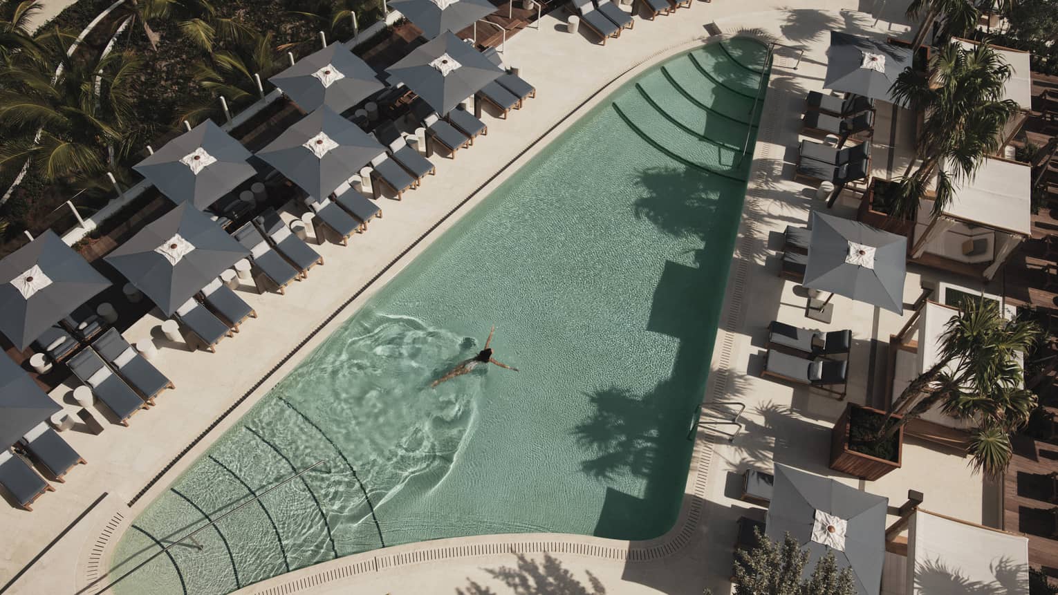 Aerial view of an outdoor pool surrounded by grey lounge chairs and umbrellas, creating a relaxing atmosphere.