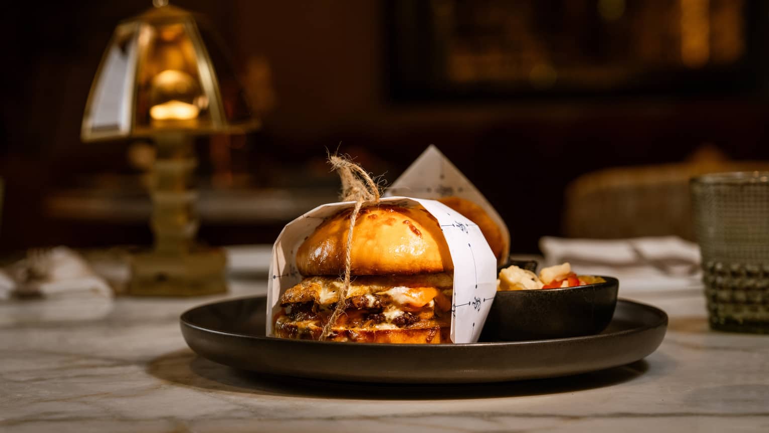 The Chicago Crusher burger wrapped in paper and string and plated on a black stoneware dish