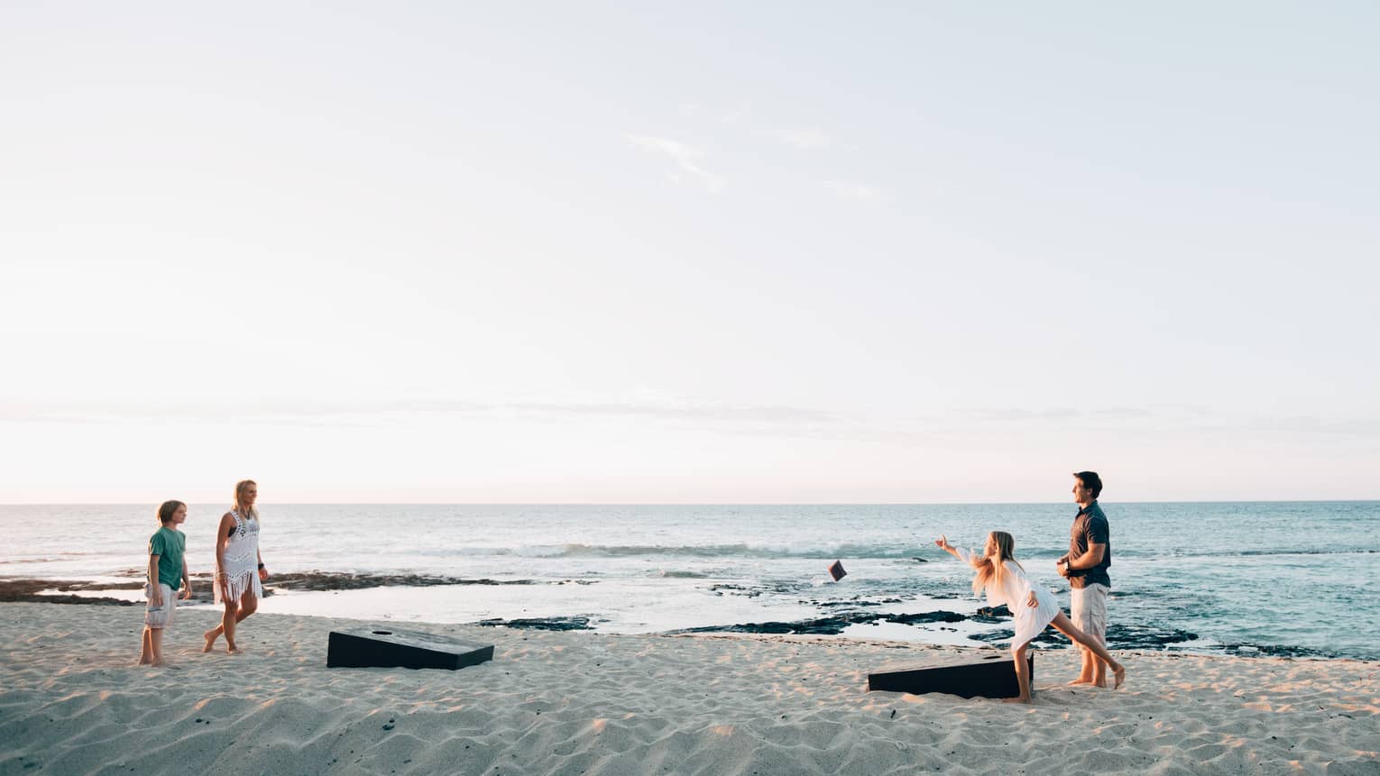Family of four plays bean bag game on sand beach by ocean