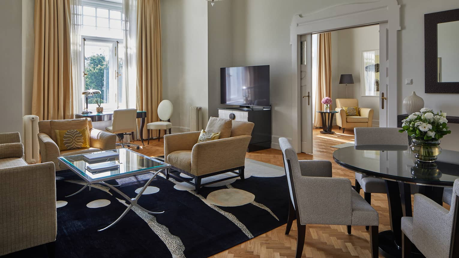 A room with round table and chairs, a sofa and coffee table, open window and a television.
