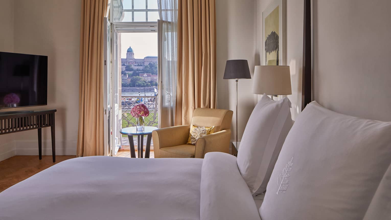 Elegant hotel room with plush bed, armchair and balcony view through tall curtains