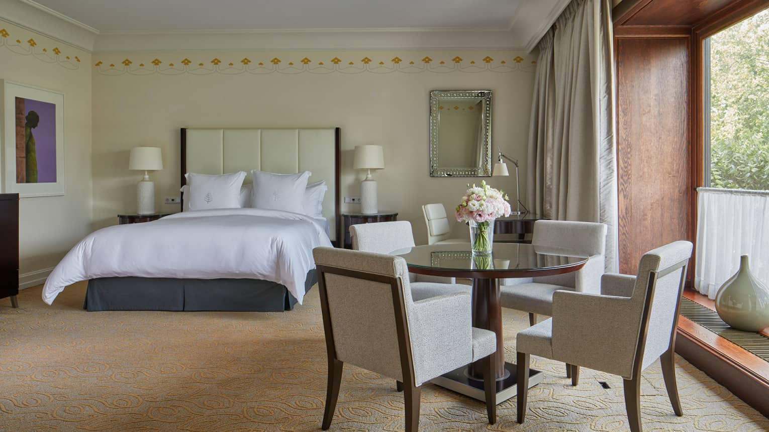 A room with a round table and four chairs, a window and bed.