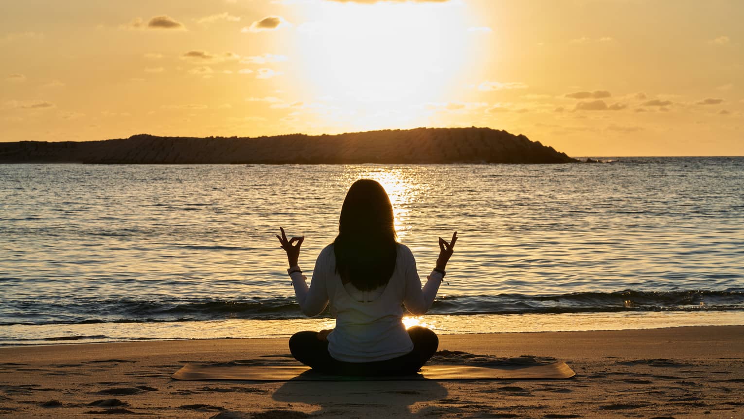 Woman meditates beachside at sunset