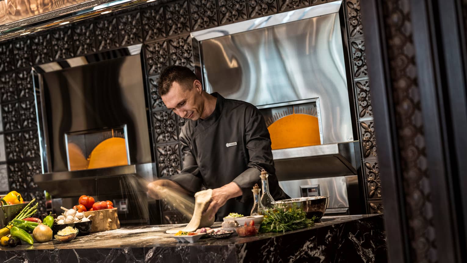 Chef in black uniform prepares dough on black marble counter