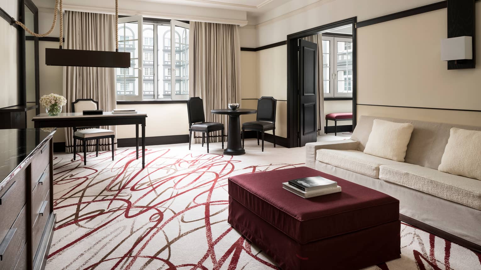 Executive Suite large burgundy ottoman with book by white sofa, white-and-red area rug