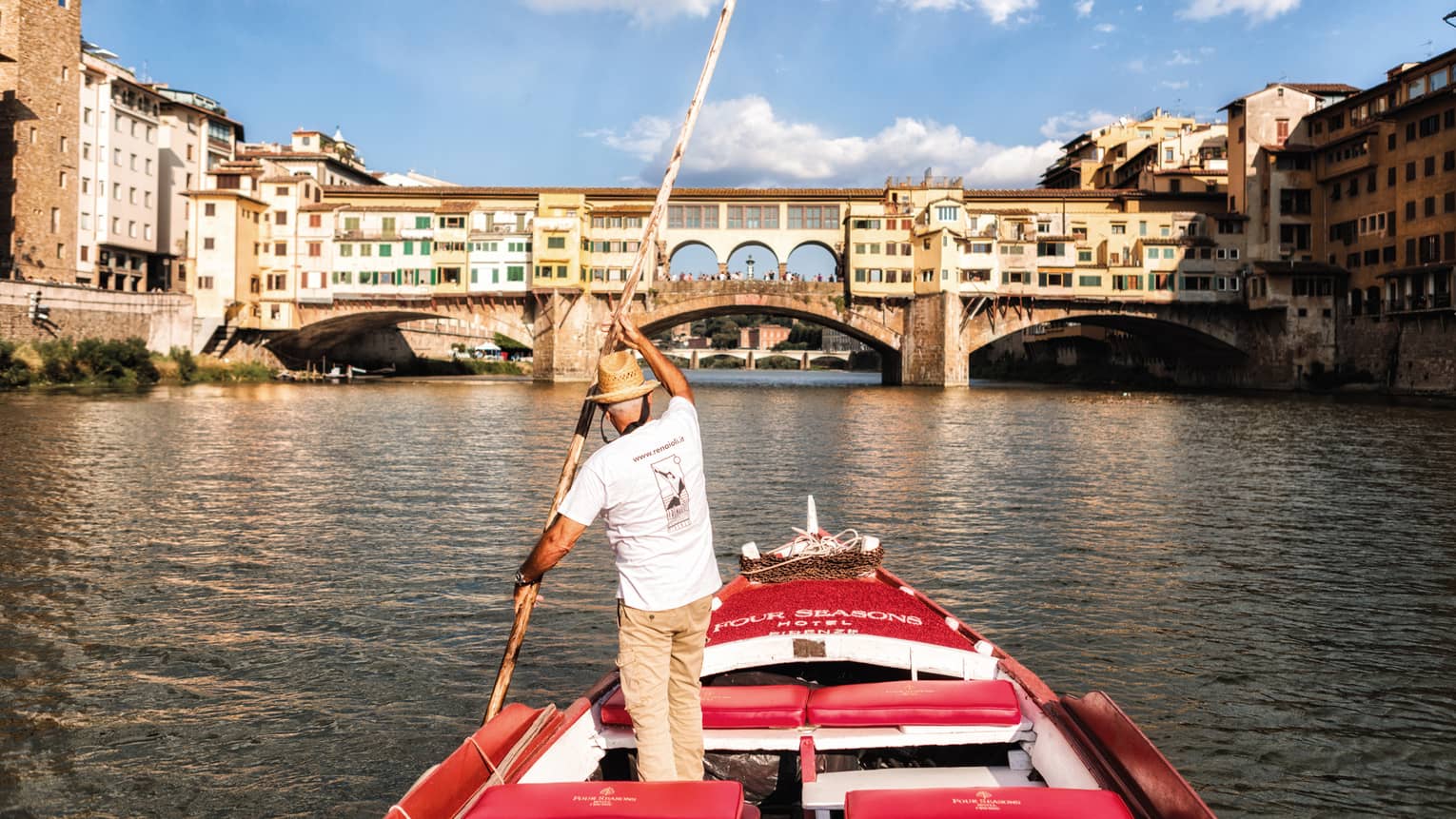 Man with long paddle steers Barchetto boat on Florence canal near bridge