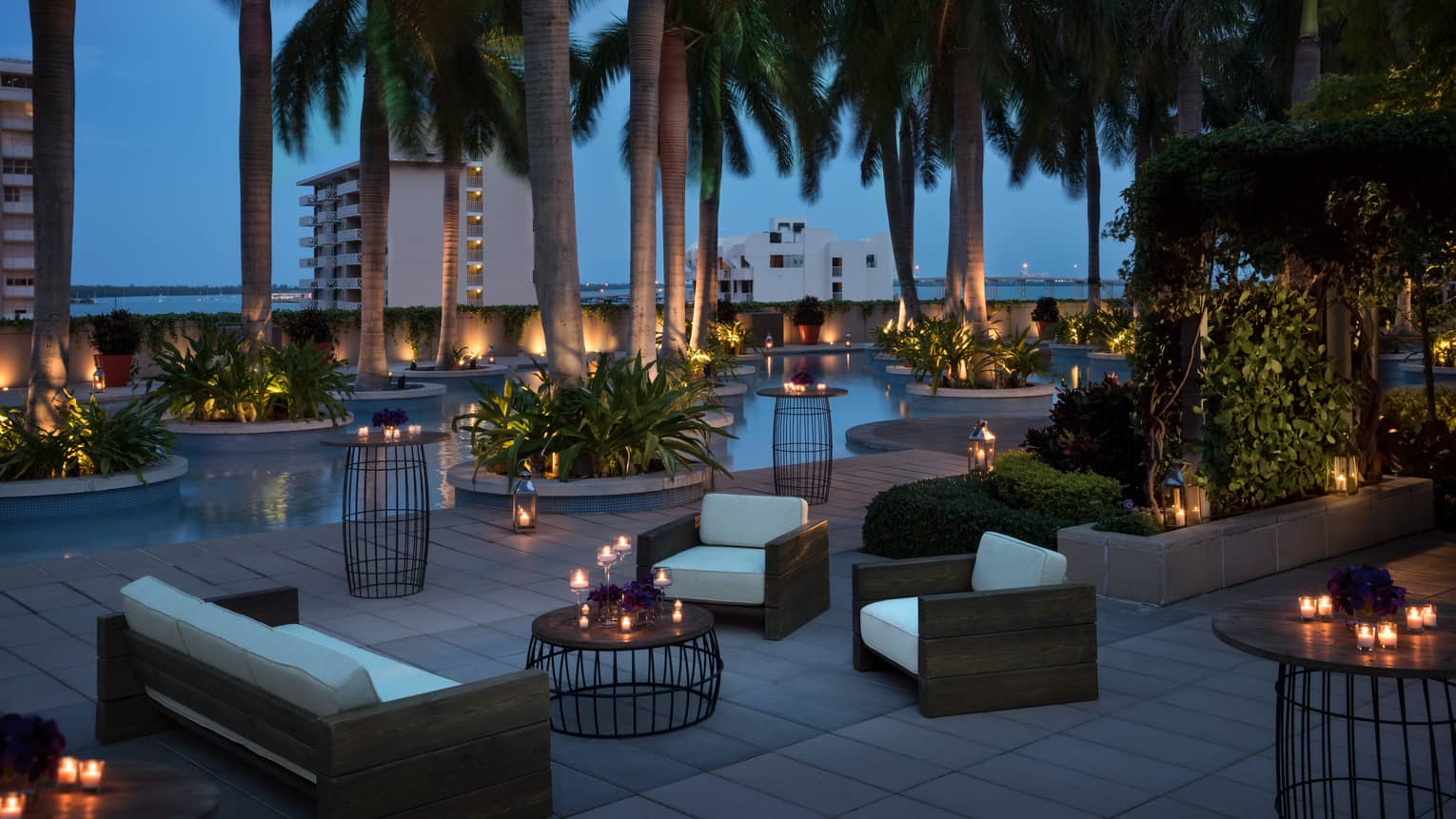 Plush white patio sofas and chairs, candle-lit tables under palm trees at night