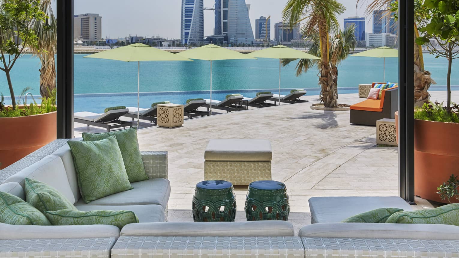 Plush outdoor patio seating and pillows under cabana, infinity swimming pool and Arabian Gulf in background