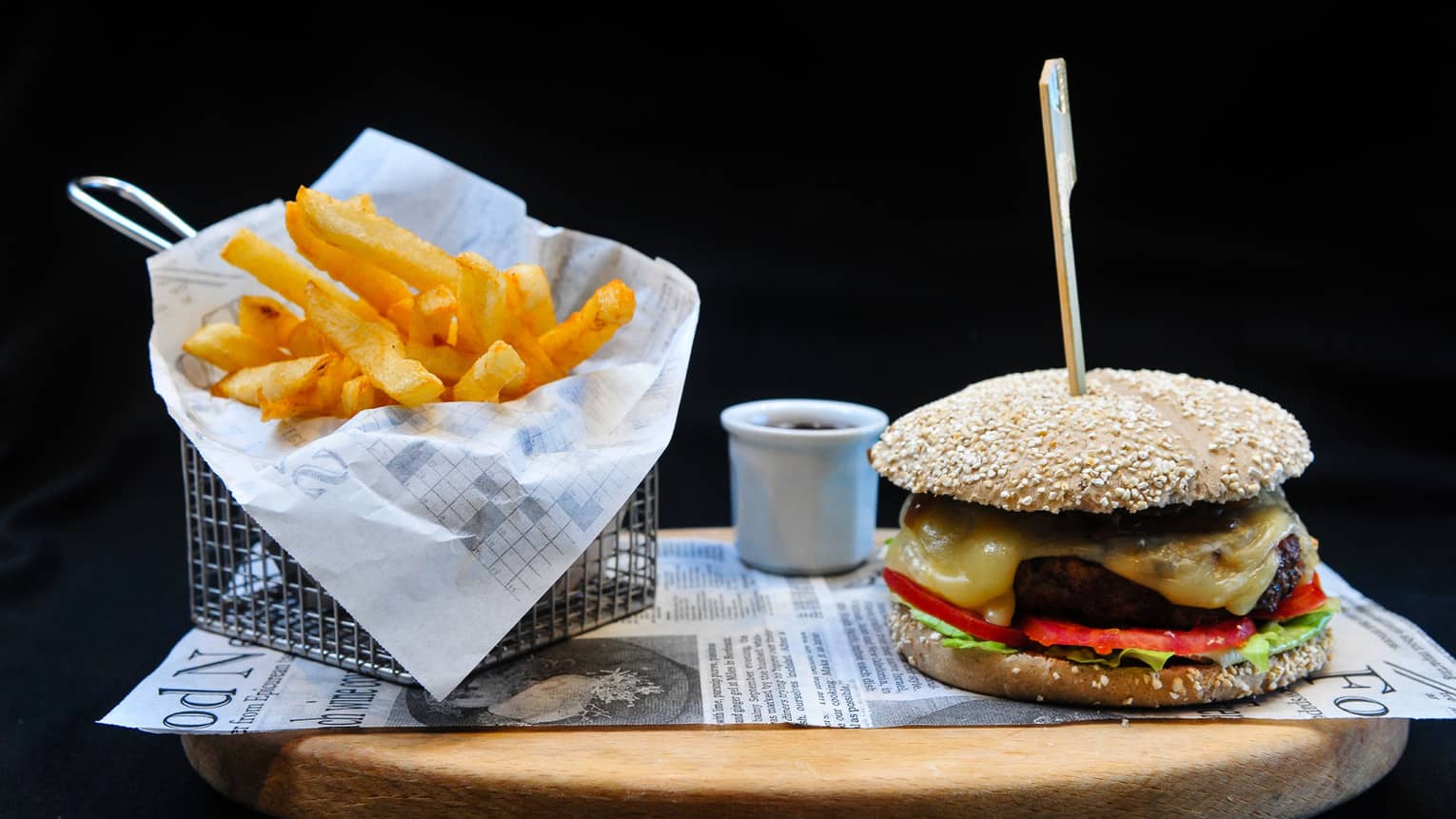 A burger with lettuce, tomato and cheese sits on a tray next to a basket of french fries