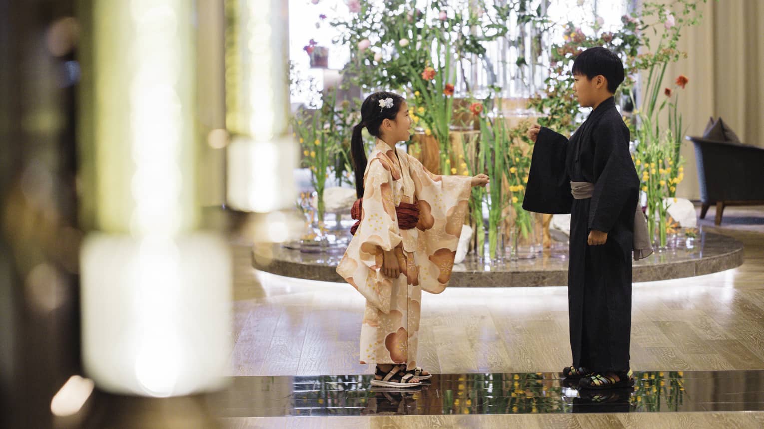 Two children dressed in yukatas stand in hotel lobby in front of elaborate floral floor display