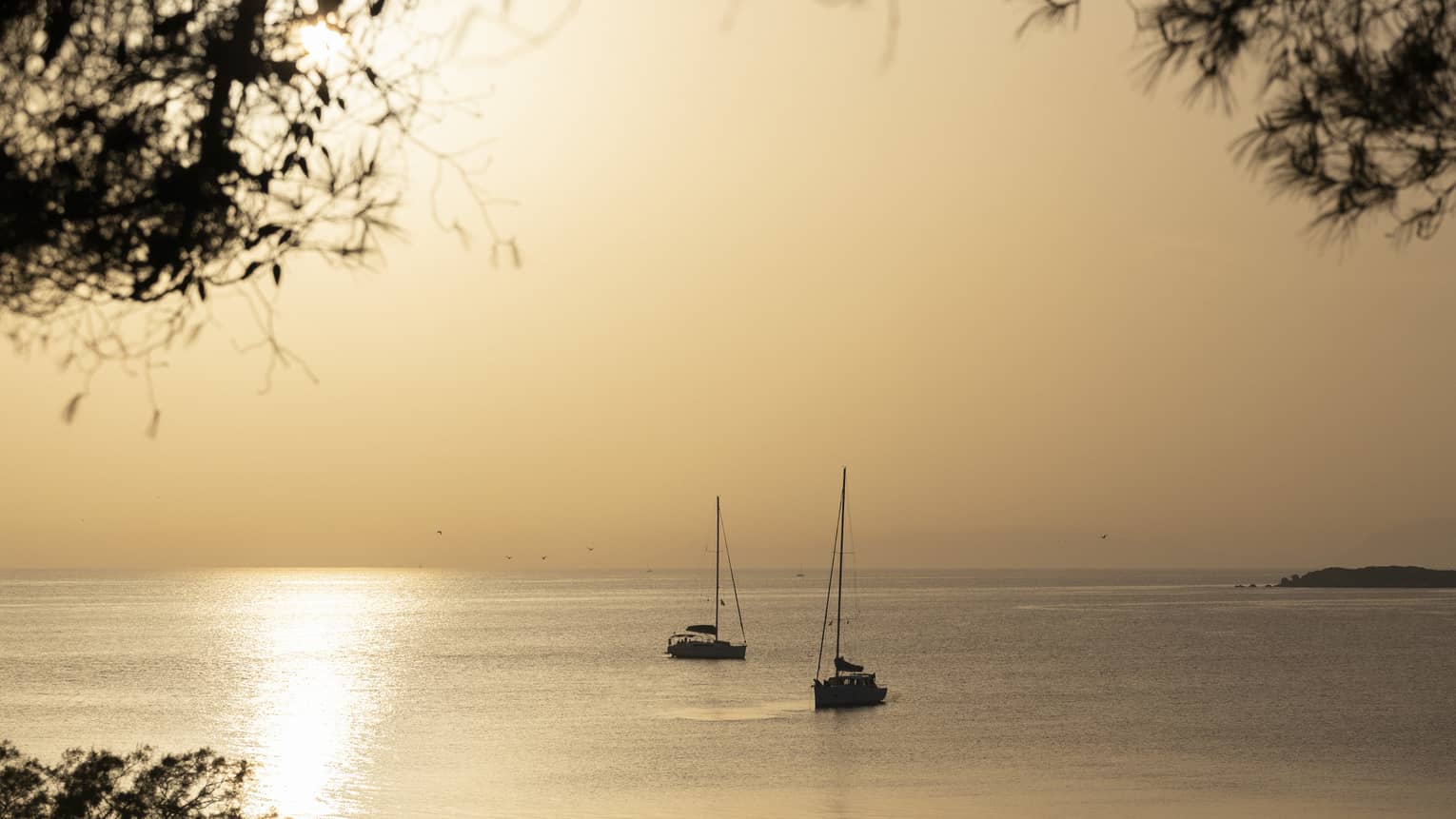Silhouette of two sailboats at dusk on ocean cruising Greek isles. 