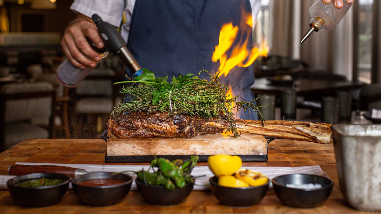 A chef using a blowtorch and oil to cook meat.
