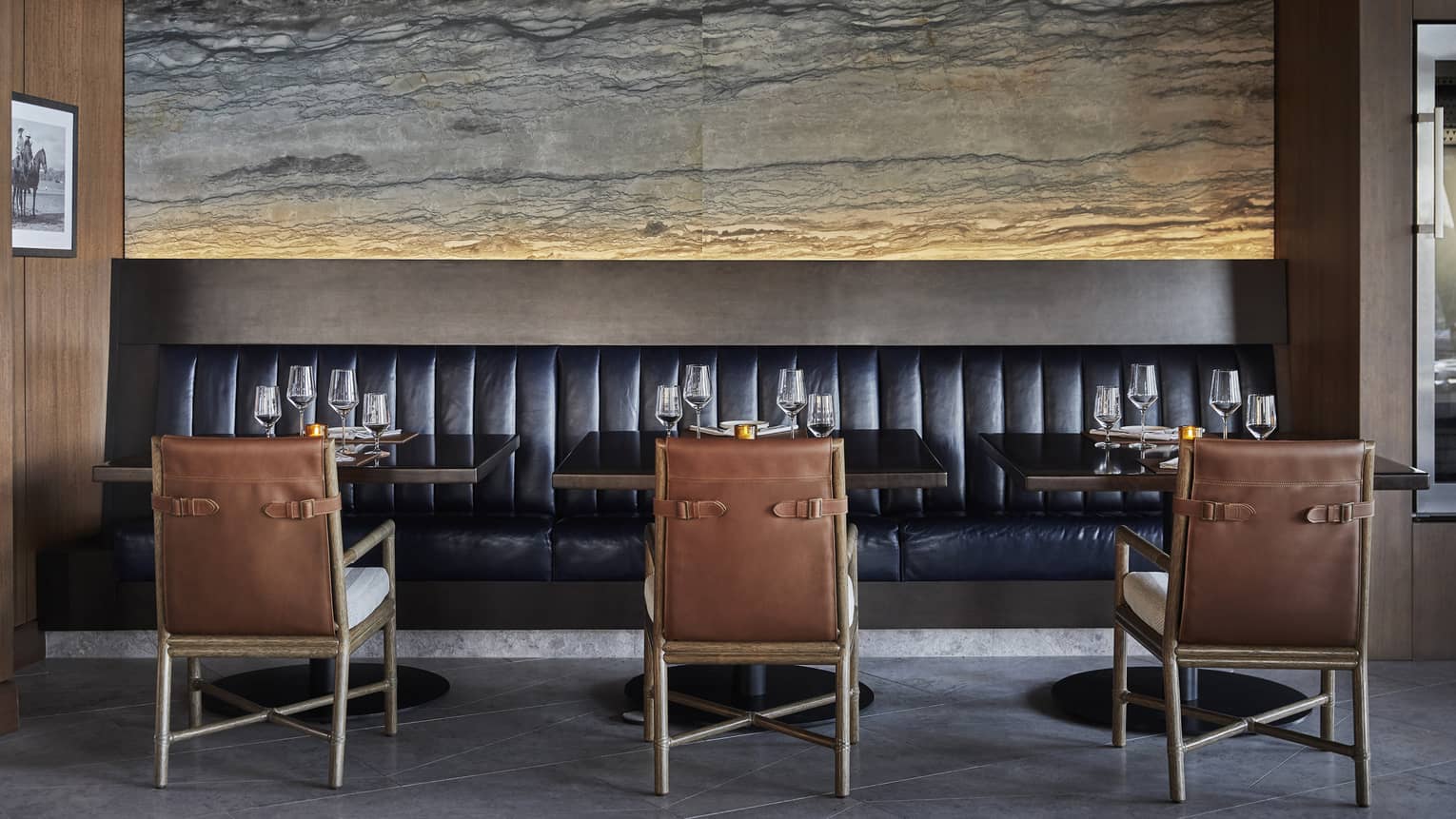 Three brown chairs face a black booth in a dining room.
