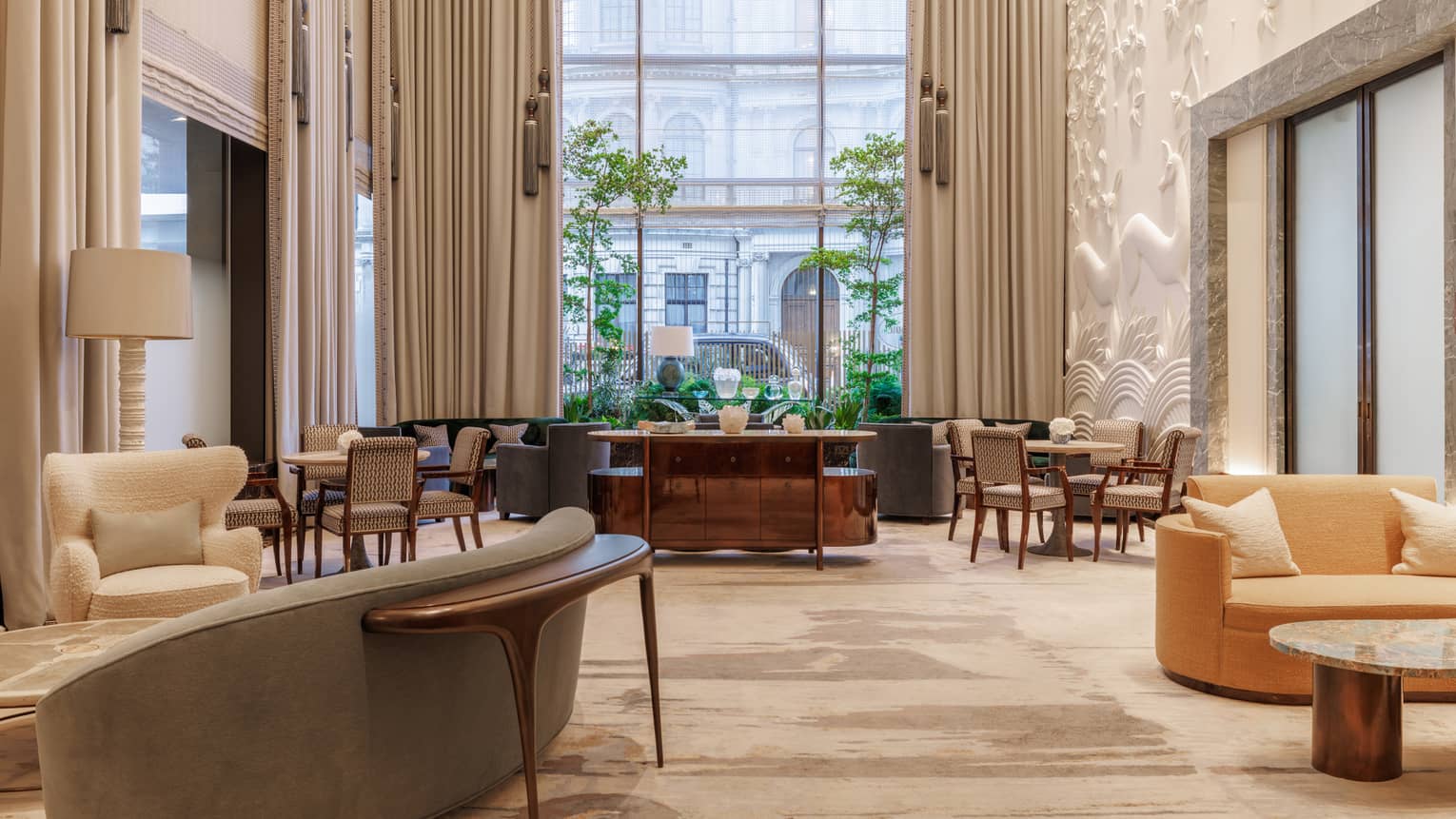 A bright, airy and spacious indoor lounge space with neutral-toned decor, comfortable seating, tables, and large windows