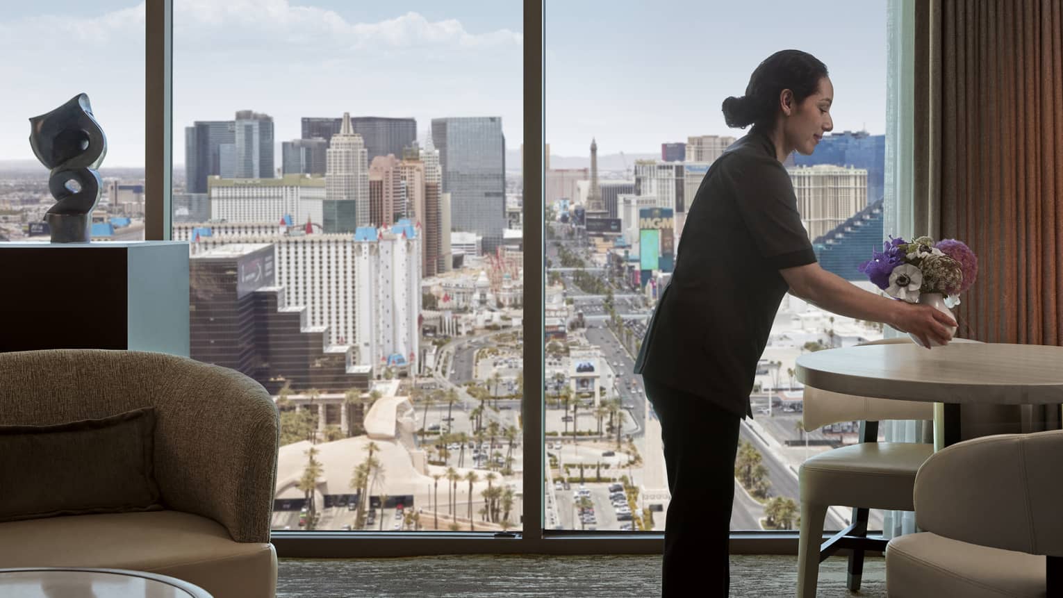 A hotel team member working in a guest room with a large window.