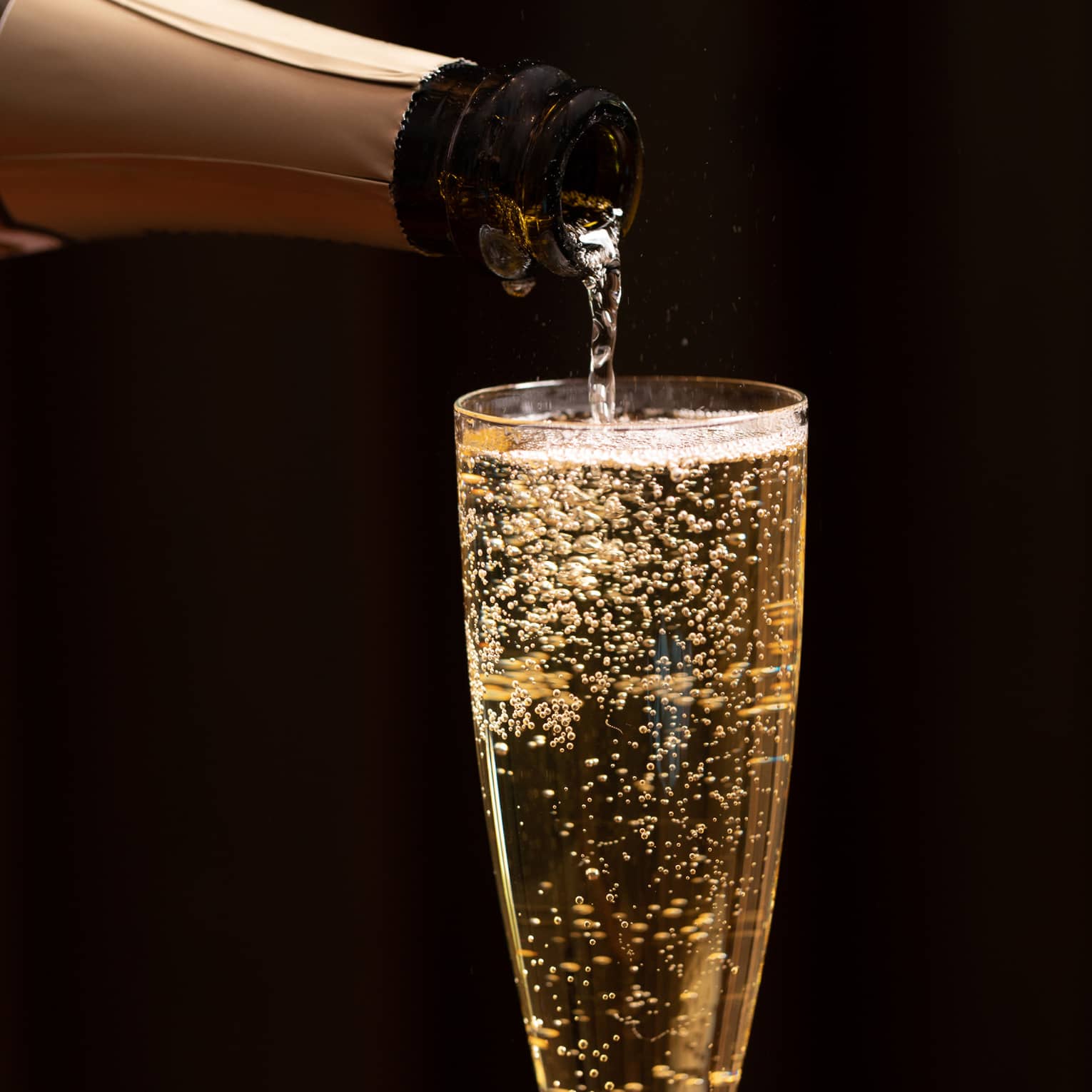 A bottle of champagne is poured into a glass as bubbles float to the top