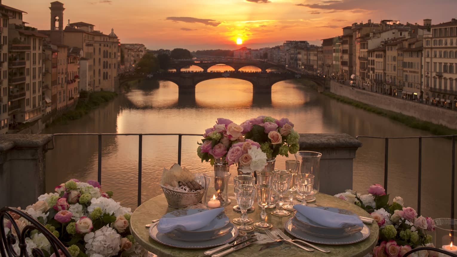Pink roses in vases on formal dining table on bridge overlooking canal, sunset