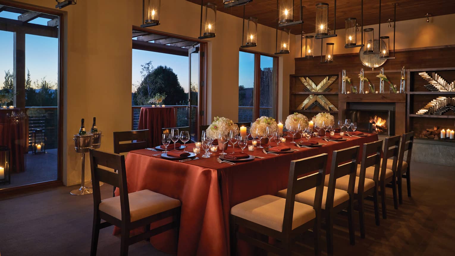 Elegant dining table set with wine glasses and flowers, lanterns hanging from ceiling, wood-burning fireplace