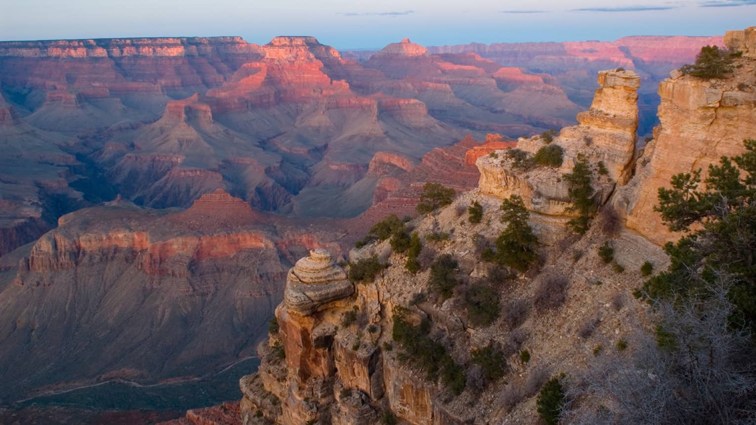 Sweeping view of Grand Canyon cliffs, canyon ridges, pink light from sunset