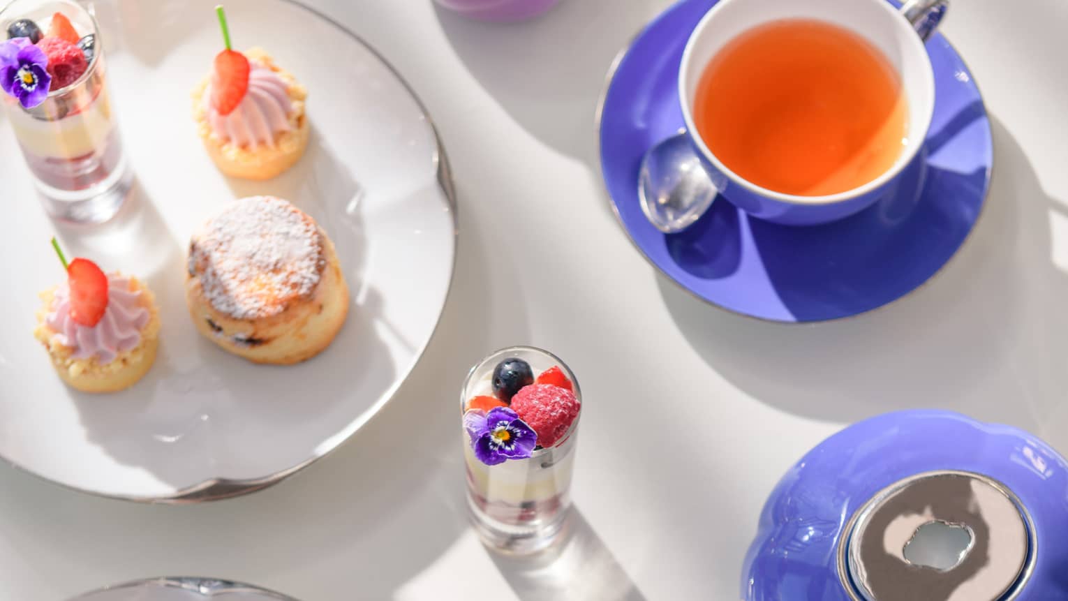 Aerial view of tea spread with plates of desserts and periwinkle-coloured cups and saucers
