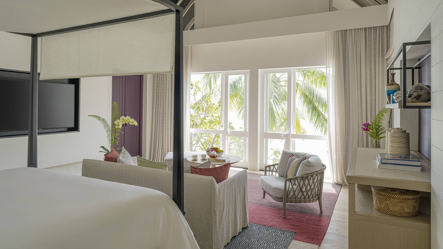 Luxury resort bedroom with four-post king bed, siting area and view of palm trees