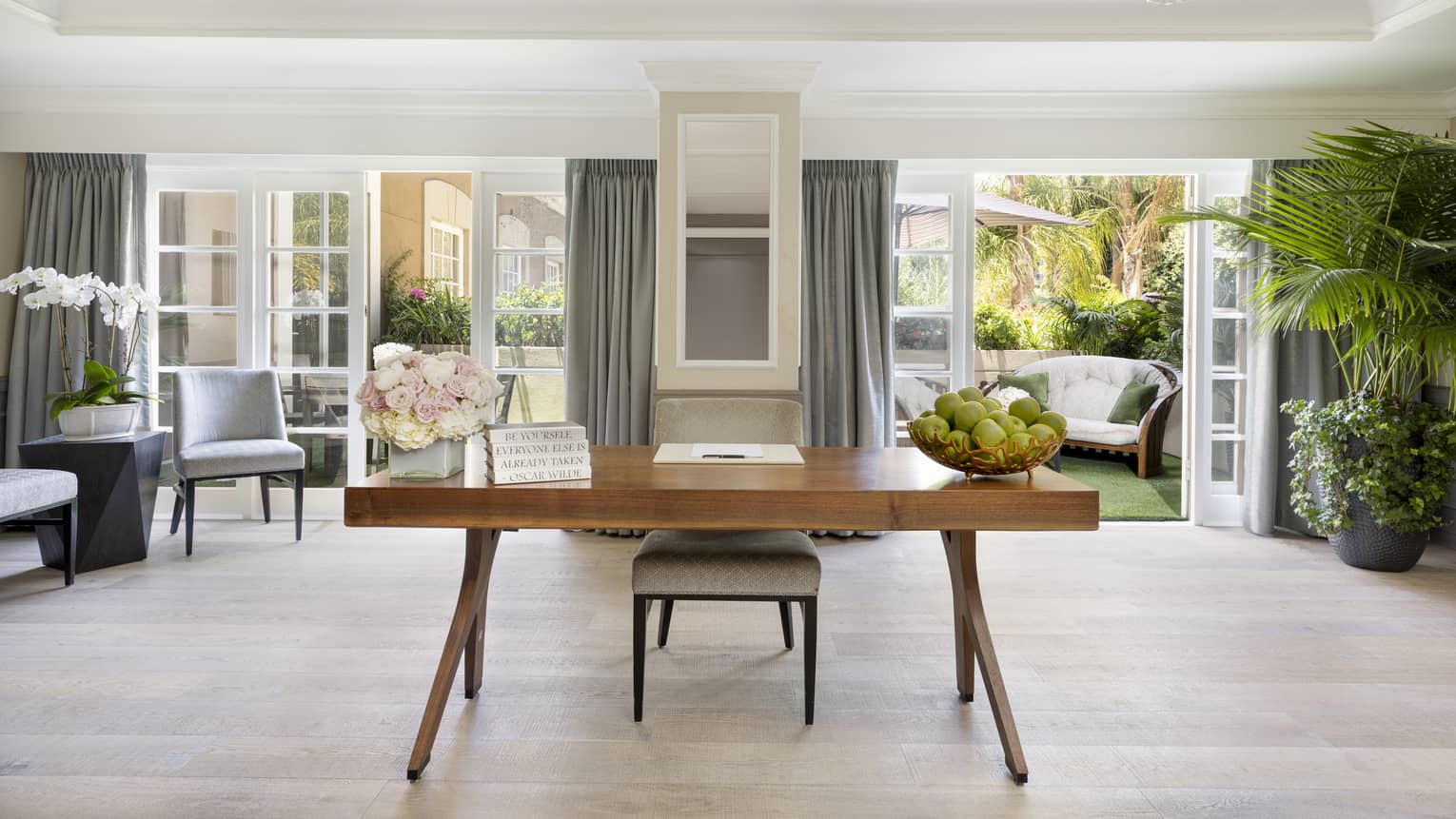 A desk in a room with plants and open patio doors leading outside.