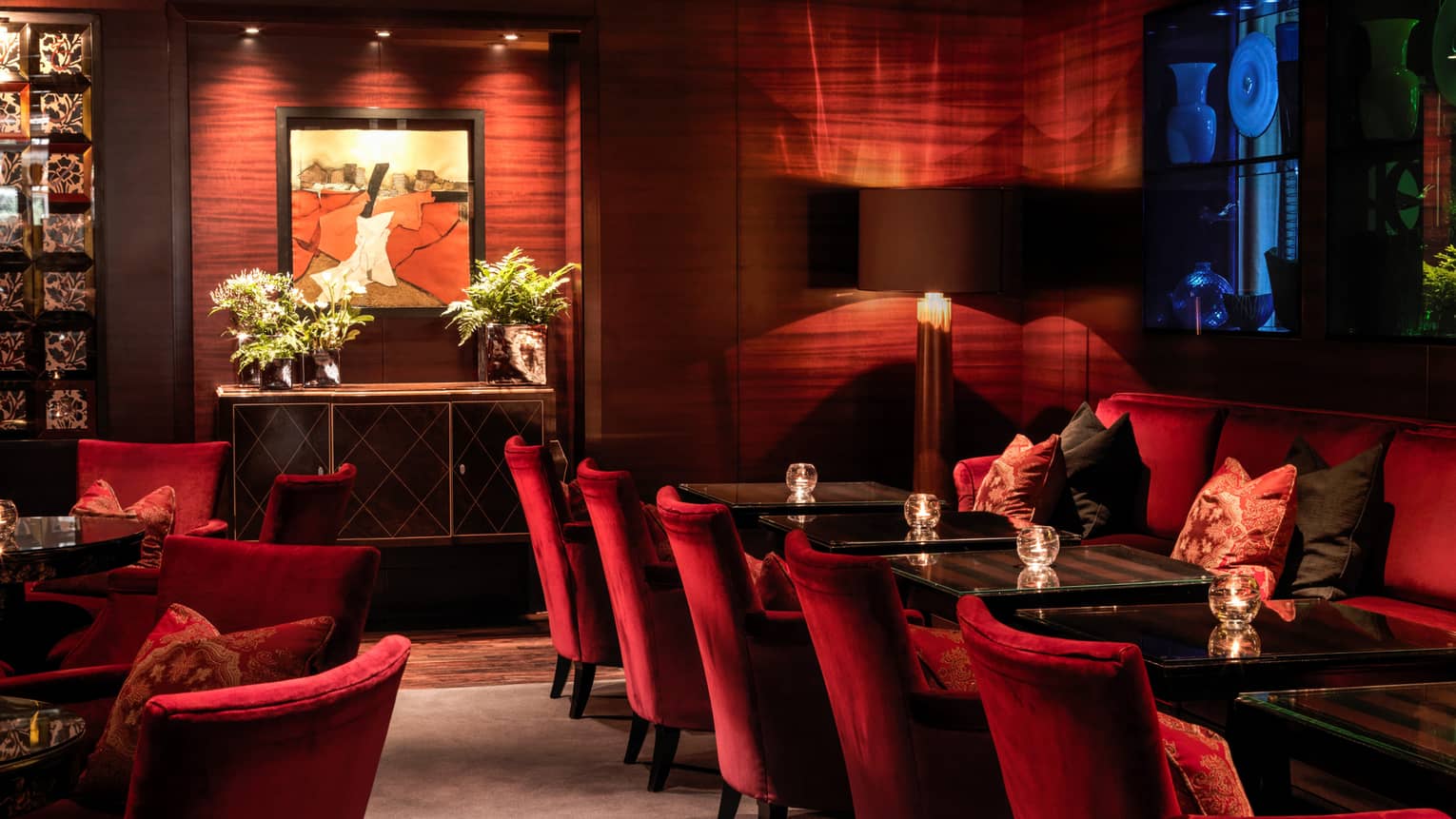 Red velvet chairs along Amaranto Lounge dining tables, modern wood walls, art, dim lighting