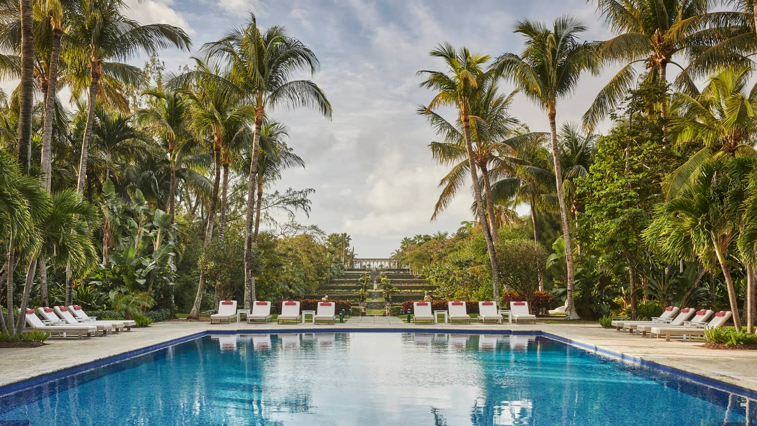 Luxury resort pool area with lounge chairs, surrounded by palm trees and lush greenery 