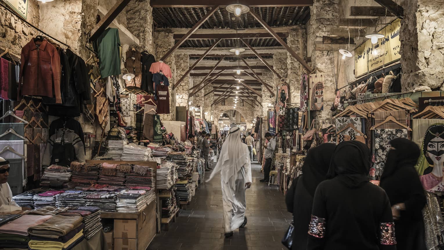 People walk past tables with textiles, clothes in indoor market