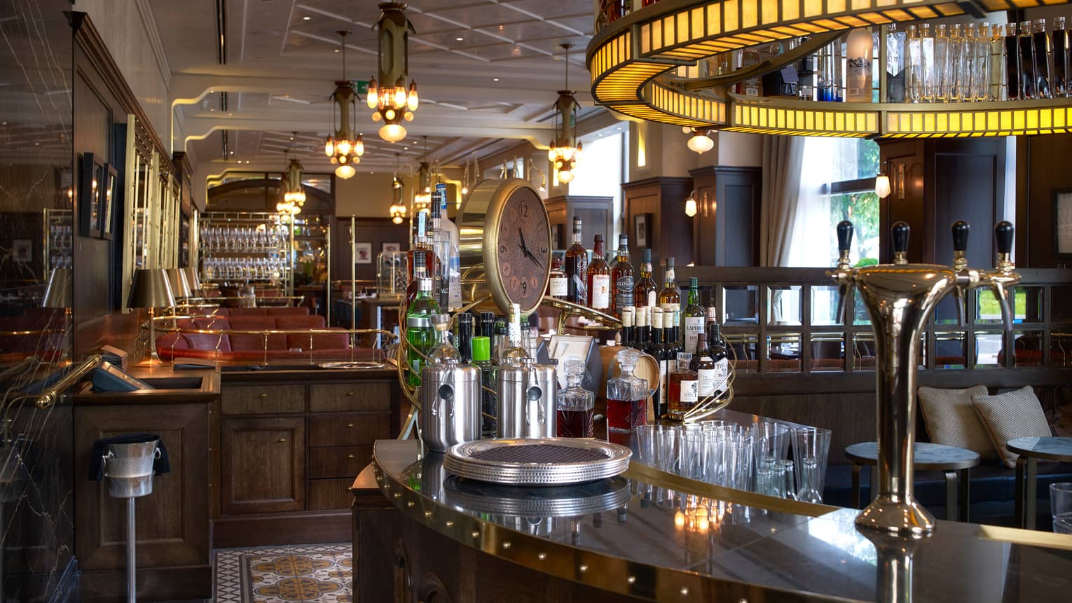KOLLÁZS Brasserie & Bar curved wood bar with round light overhead, large clock, wine bottles
