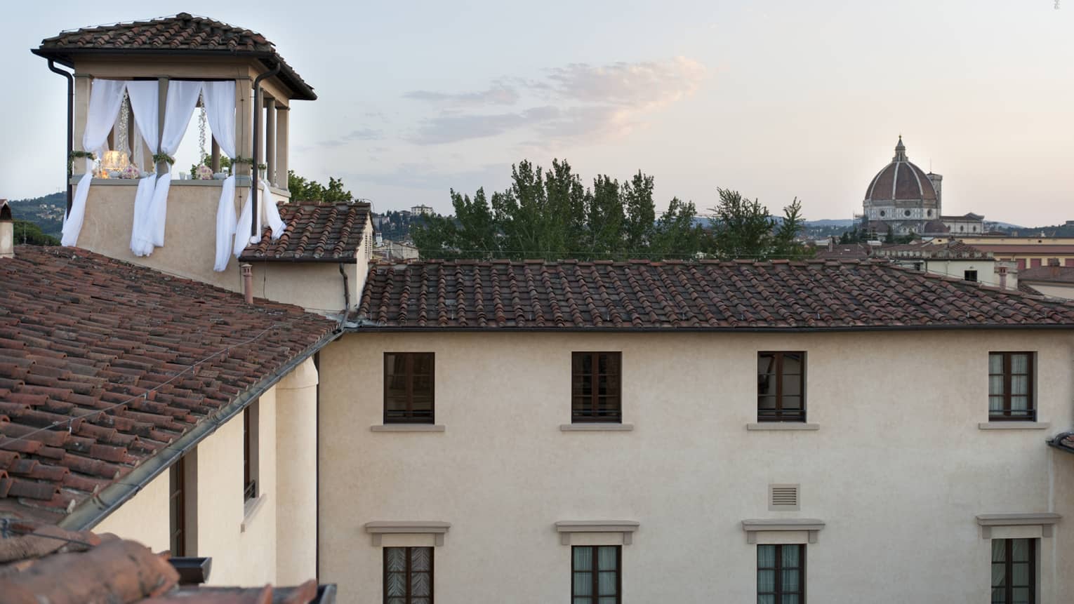 Looking across the red tiled rooftop of the Hotel to a small terrace with white flowing curtains and romantic decorations.