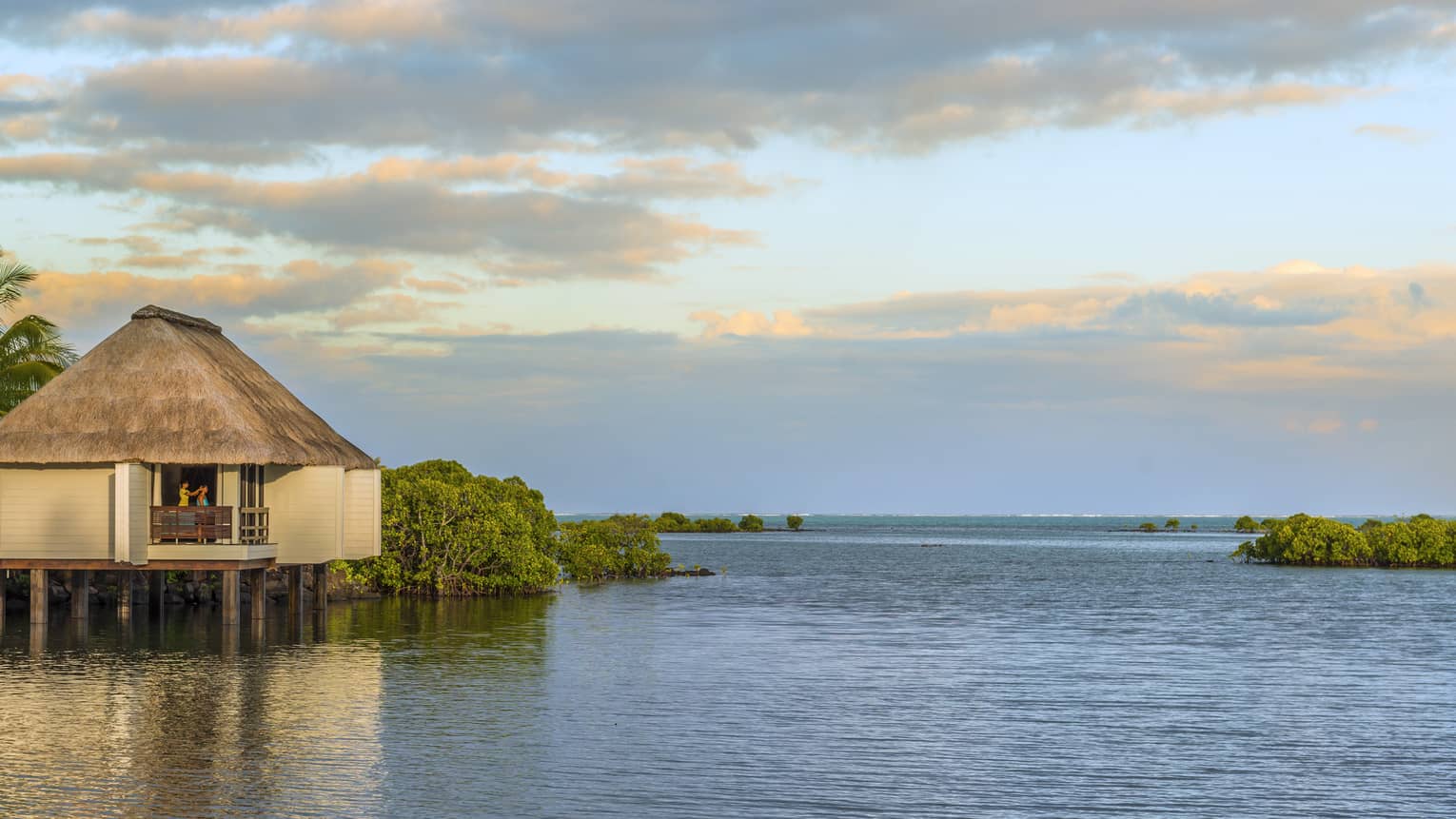 Overwater spa villa with thatched roof at sunrise