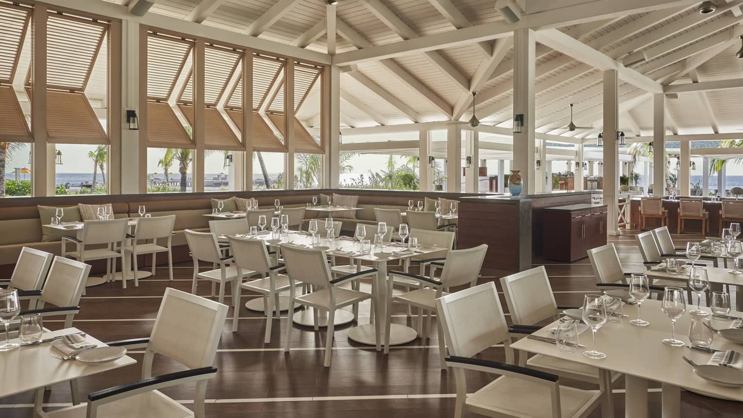 Indoor-outdoor restaurant with glass tables, white chairs, wooden beamed roof 