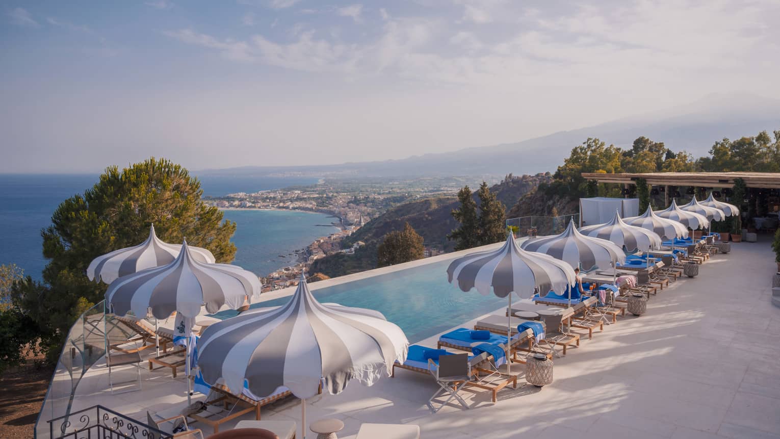 Long rectangular infinity pool with playful striped umbrellas, view of coastline