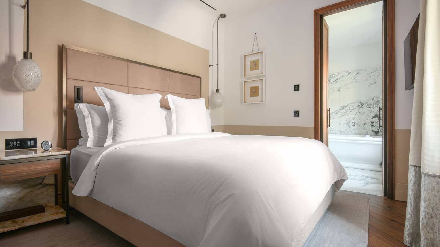 A bed in a room with white sheets next to a side table and lamps.