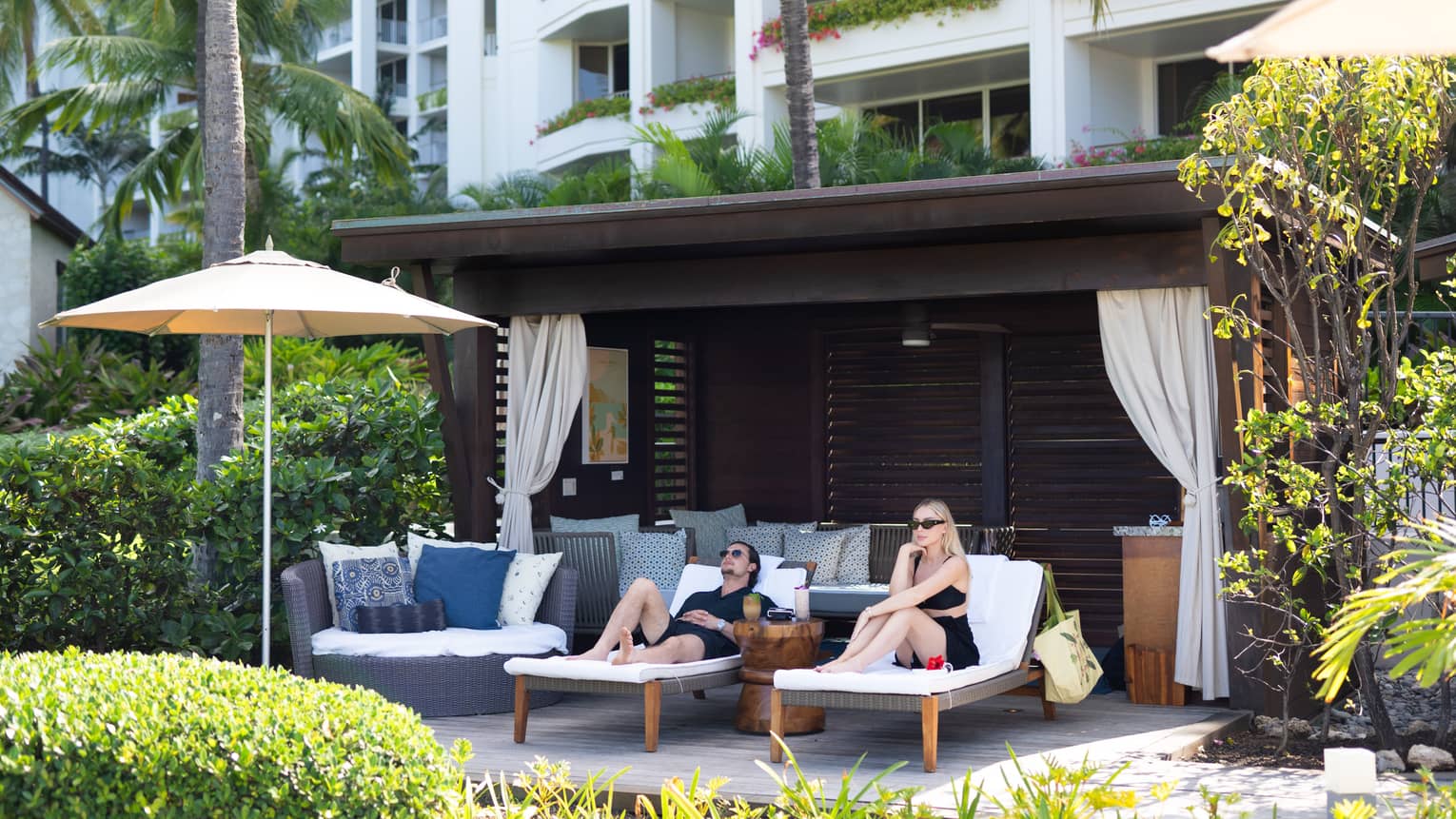 Man and woman lounge on sun chairs under private cabana