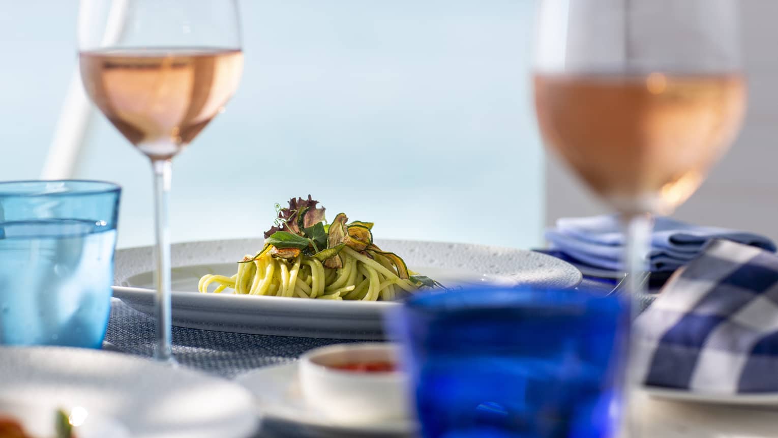 A side view of a table with glasses of rose and a pasta dish over looking the ocean in Four Seasons Maldives - Landaa