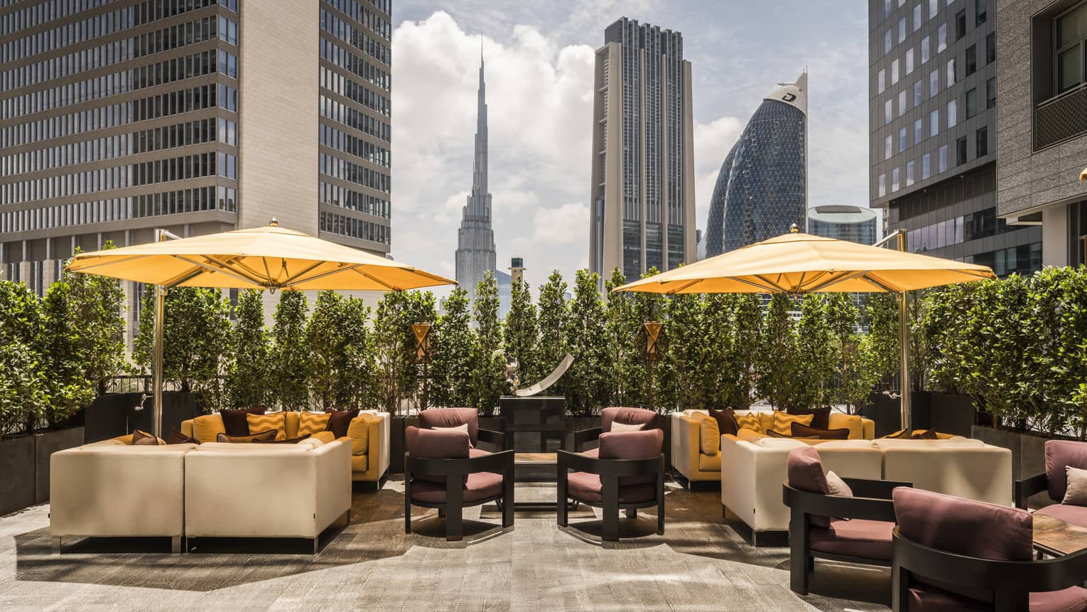 Sunny Penrose Lounge patio with white sofas and chairs, large yellow umbrellas, Dubai skyline