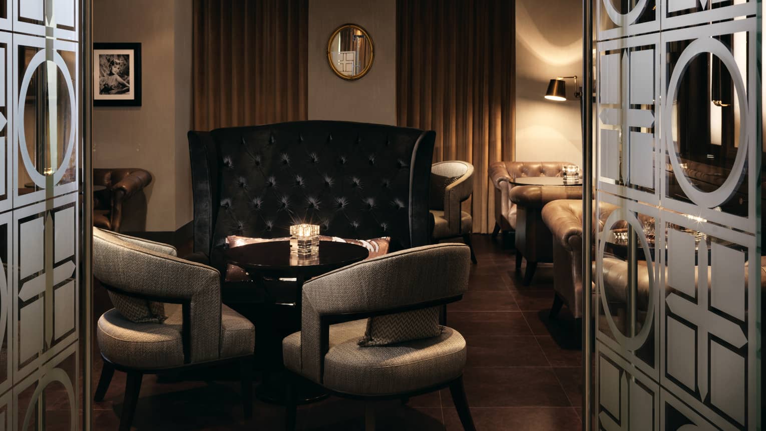 View through decorative glass doors to cocktail table, chair in dimly-lit Zsa Zsa Cigar Bar 