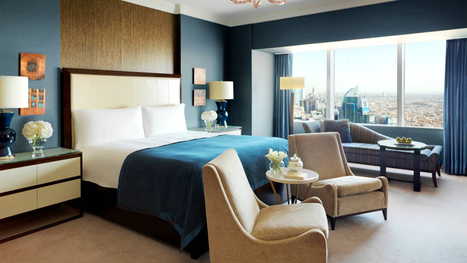 Presidential Suite with bright blue and beige decor, tall wood panel behind headboard, two armchairs, chaise