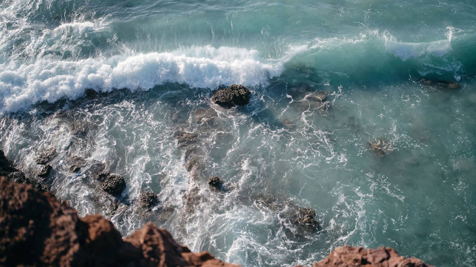 Aerial view of an ocean wave breaking over a rock formation